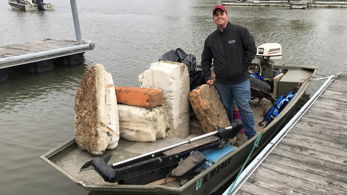 A student stands on a boat with trash he removed from the lake. 