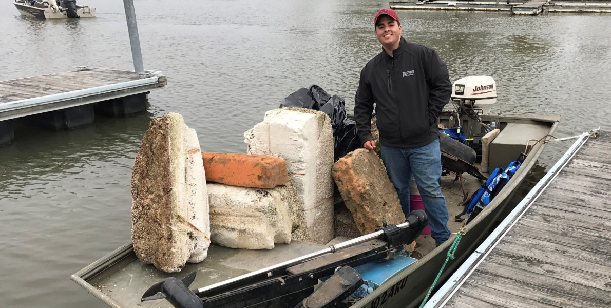 A student stands on a boat with trash he removed from the lake. 